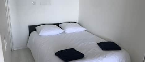 A single bed with white bedding and two pillows, a dark headboard, and a folded dark towel on the footboard.