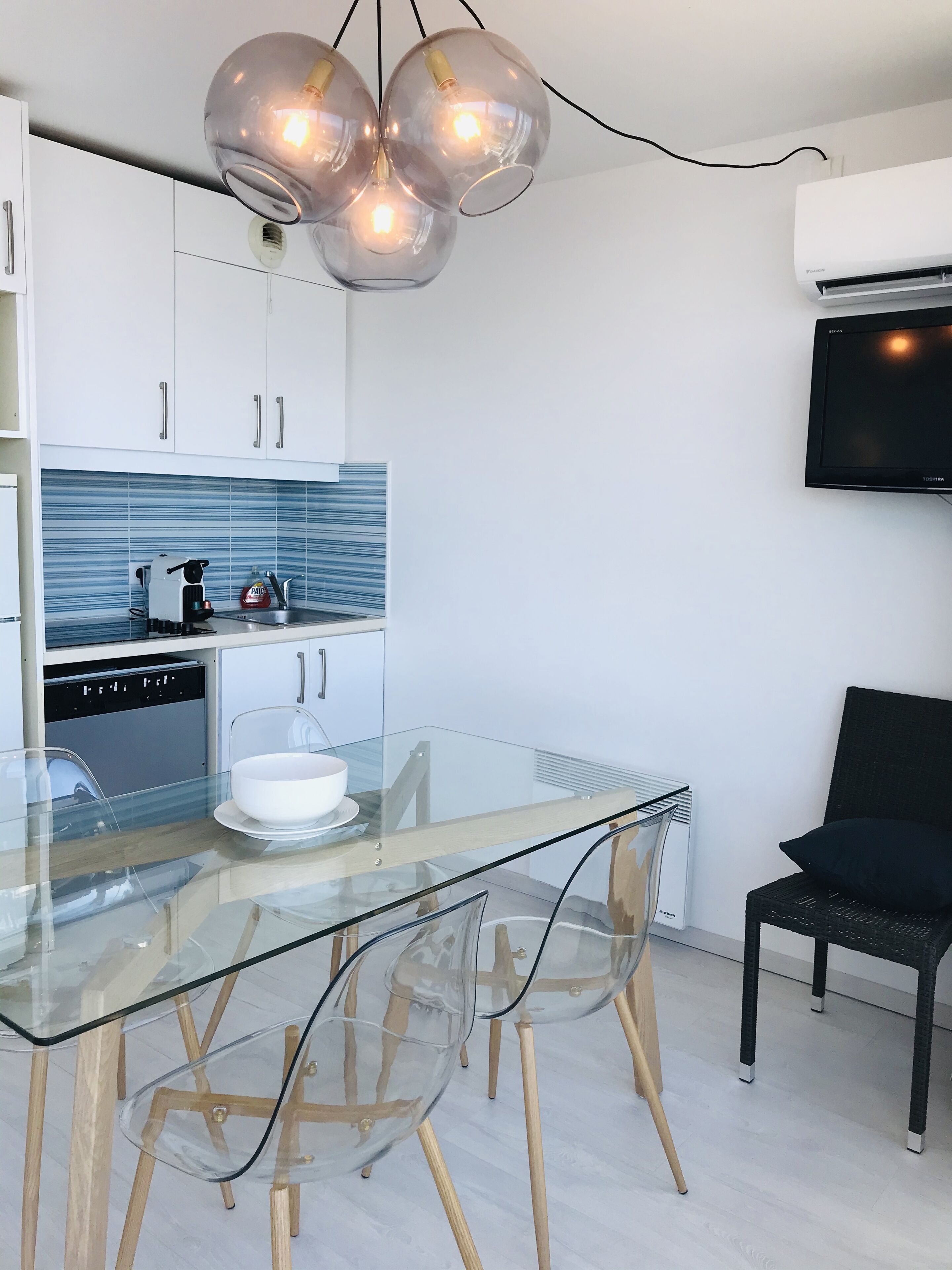 A modern kitchen with a glass dining table, clear chairs, and a unique spherical pendant light.