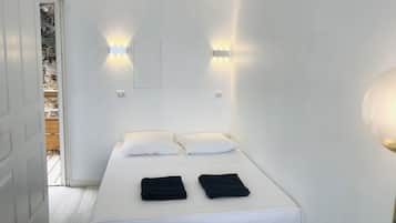 Un lit simple avec une literie blanche et deux serviettes noires, une porte blanche et un luminaire fixé au mur.