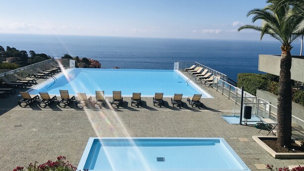 A pool with lounge chairs and a view of the ocean.