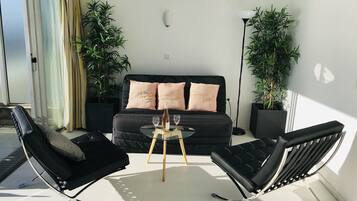 A modern living room with a black sofa, two black lounge chairs, a glass coffee table, and two potted plants.