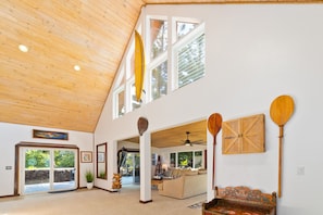 A spacious living area with a high ceiling, large windows, and a view of the outdoors.
