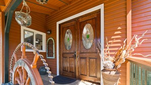 Une maison en bois avec une porte d’entrée en bois, un porche doté d’une chaise berçante et un grand vase orné de branches décoratives.