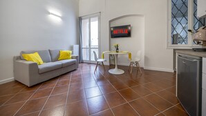 A modern living room with a grey sofa, yellow cushions, a small dining table, and a kitchen area with a dishwasher. - [Ghirlandina] Fantastic loft in the city center (Modena)