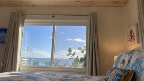 Una habitación con un ventanal grande, techo de madera y una cama con colcha estampada.