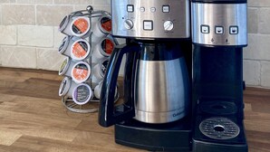 Una cocina con cafetera, un escurreplatos para tazas y un expositor para frascos de vidrio.