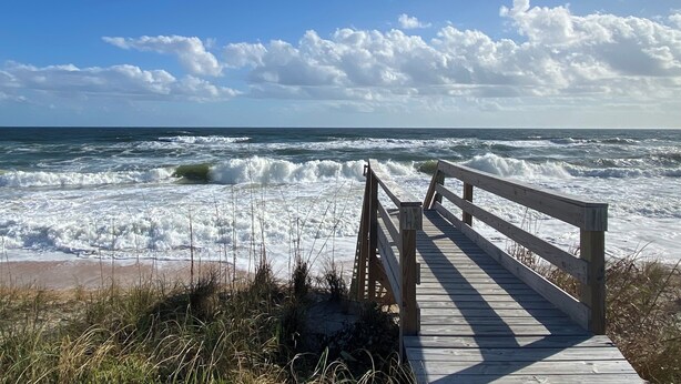 Un paseo marítimo de madera que conduce al océano, con olas rompiendo en la orilla.