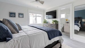 A bedroom with a bed, a ceiling fan, a TV, and a view of the outside.