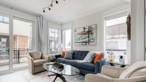 A modern living room with a sofa, armchairs, a glass coffee table, and a large window.