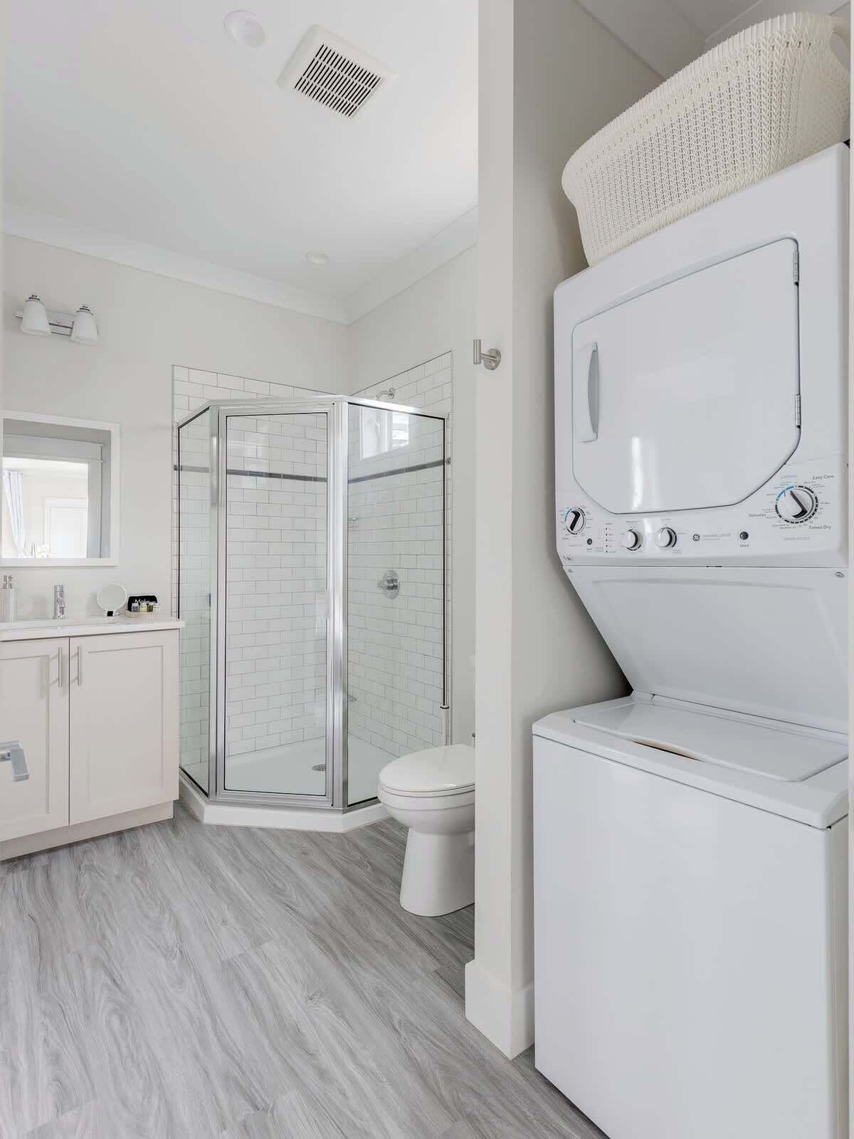 A modern bathroom with a glass shower enclosure, a toilet, and a stacked washer and dryer.