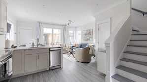 A modern kitchen with a central island, a dining area with a table and chairs, and a staircase leading to another level.