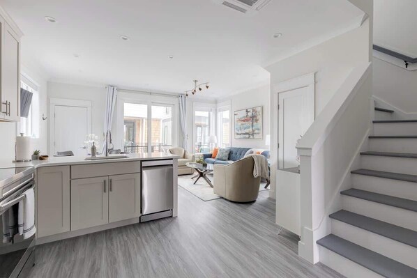 A modern kitchen with a central island, a dining area with a table and chairs, and a staircase leading to another level.