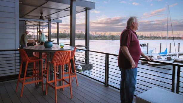 A covered outdoor area with a table and chairs, a railing, and a view of a body of water with boats.