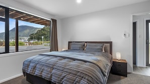 Un dormitorio con una cama grande, una mesita de noche, una lámpara y vistas a una montaña y al paisaje a través de una ventana.