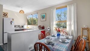 Una cocina moderna con armarios blancos, un refrigerador, microondas y estufa. Hay un comedor con una mesa lista para cuatro personas, rodeada de sillas de madera.
