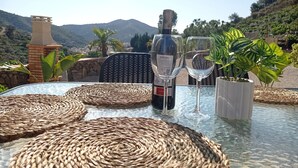 A table with a bottle of wine and two glasses, surrounded by woven placemats, set against a scenic mountain backdrop.