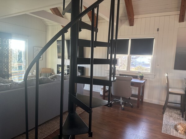 A modern living room with a black metal staircase, a grey sofa, a wooden desk, and a white chair. - Seaside Escape! completely renovated. Ocean views steps to private beach (Rodanthe)