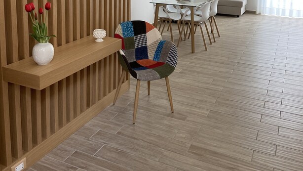 A modern living room with a wooden slatted partition, a glass coffee table, a colorful patchwork chair, a white sofa, and a dining area with white chairs. - Loft Crispi Refined, cozy and functional apartment. (Siracusa)