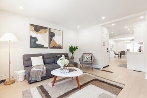 Un salon moderne avec un canapé gris, une table basse blanche et des œuvres d’art abstraites accrochées au mur.