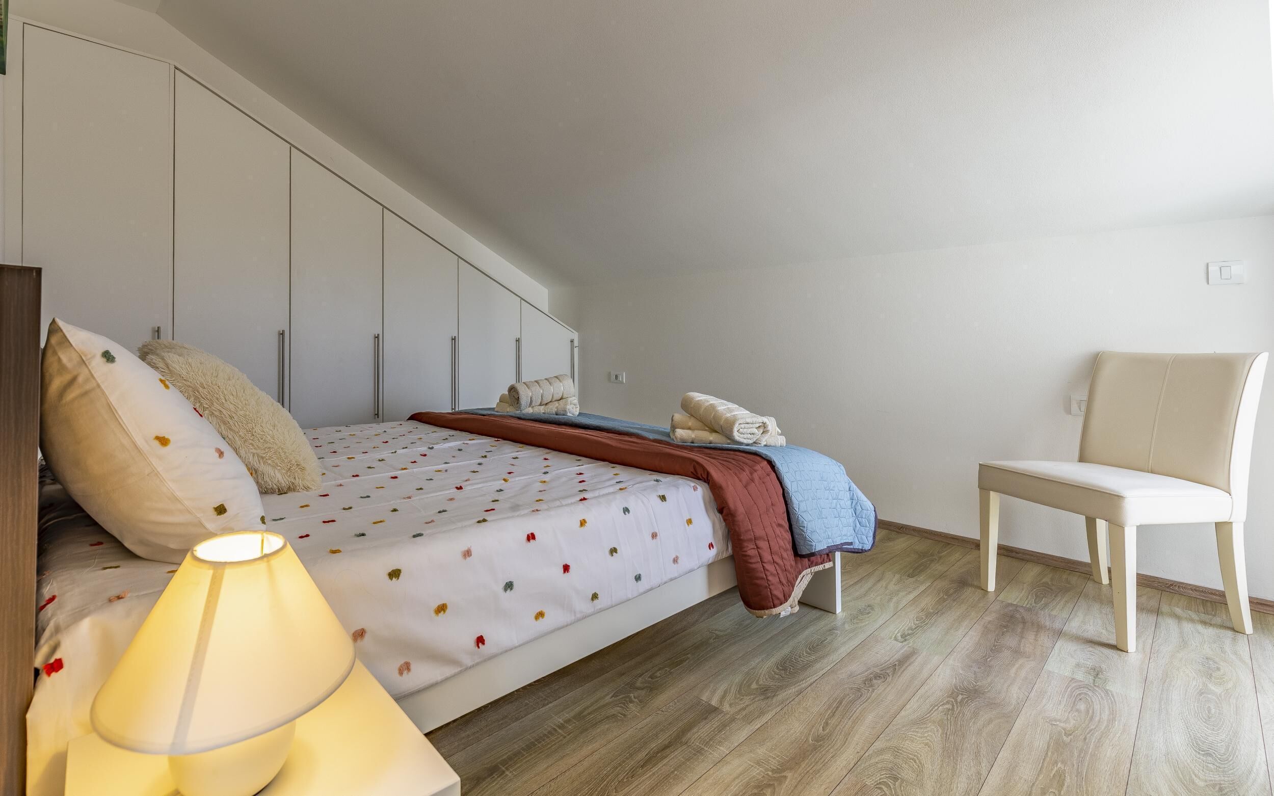 A bedroom with a bed, a chair, and a lamp.