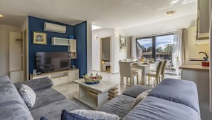 En moderne stue med et fladskærms-tv, et spiseområde med et bord dækket til to, og en balkon med udsigt.