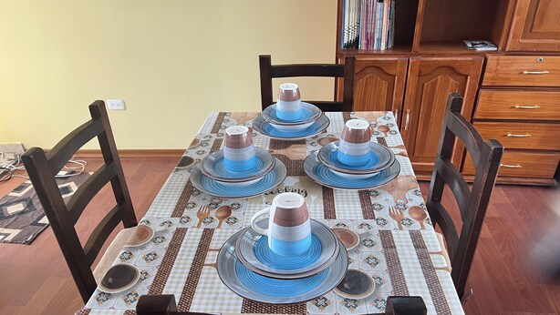 Uma mesa de jantar posta com pratos azuis e castanhos, rodeada por cadeiras de madeira.