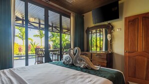 A hotel room with a bed, a wooden dresser, a mirror, and a TV mounted on the wall. - Kaluma Frog Farmstay Villa La Fortuna (San Ramon)