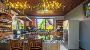 A modern kitchen with a central island, wooden chairs, and a view of greenery outside. - Kaluma Frog Farmstay Villa La Fortuna (San Ramon)