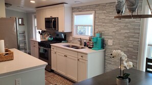 A modern kitchen with white cabinets, a stainless steel refrigerator, a microwave, and a stove. - St Augustine waterfront home on canal w/ private dock, walk to beach! (St. Augustine)