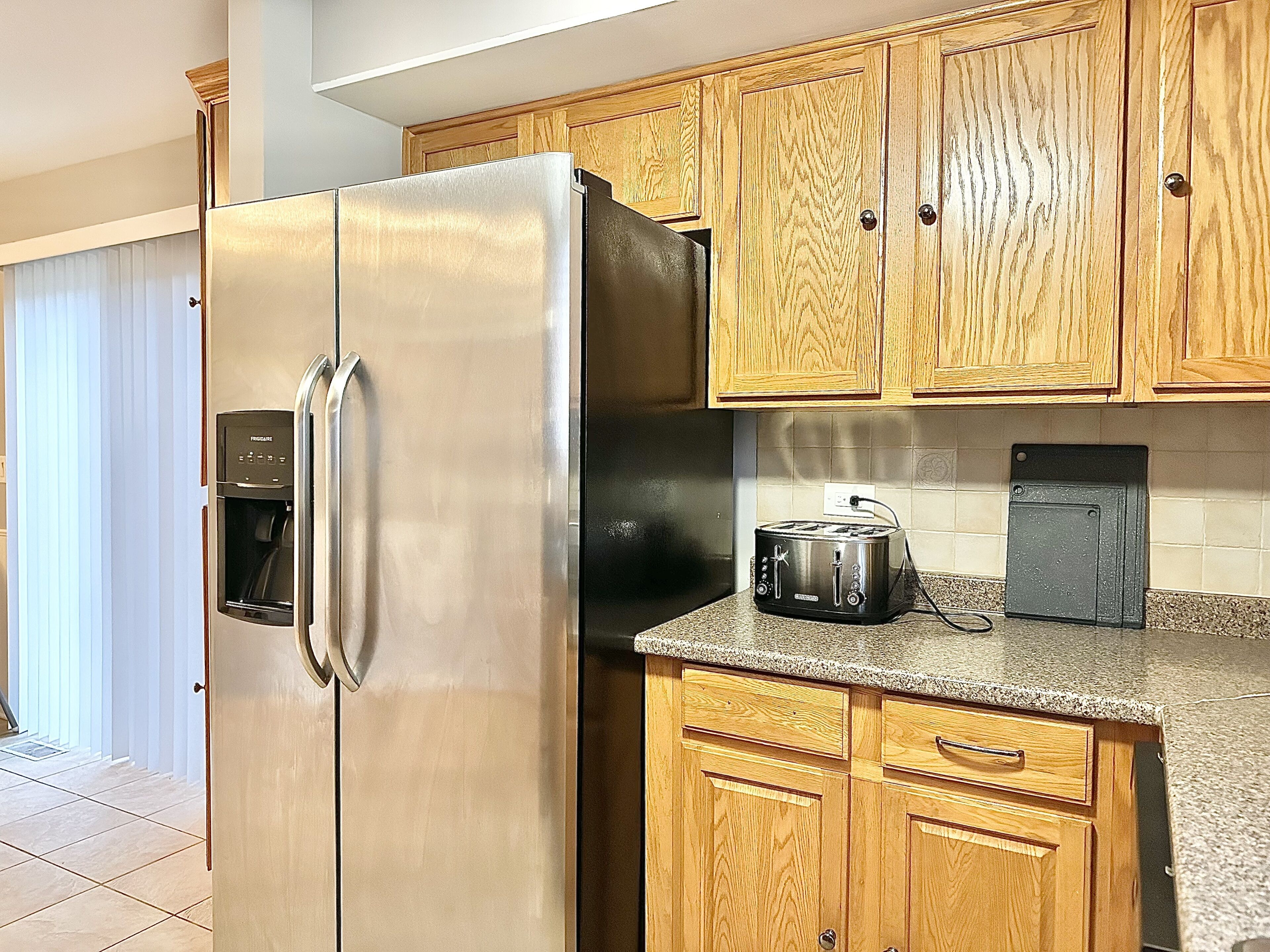 Una cocina con armarios de madera, un refrigerador de acero inoxidable, un horno empotrado y una tostadora.