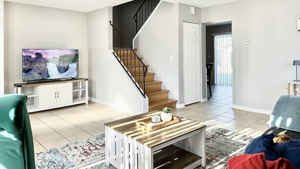 A modern living room with a staircase, a flat-screen TV, a coffee table, and a view of the outside. - Fast Wi-Fi/Comfy beds/Free parking/3bdr house/4TVs
 (Aurora)