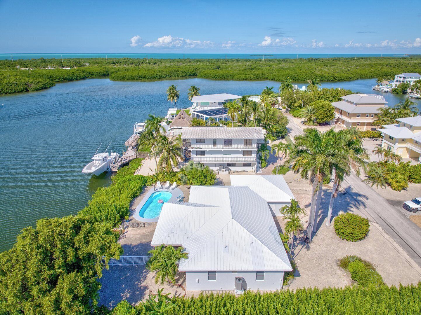 An aerial view of a coastal property with a swimming pool, multiple buildings, and boats docked near the water.
