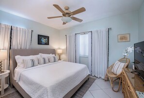 A bedroom with a large bed, a ceiling fan, and a window with curtains.