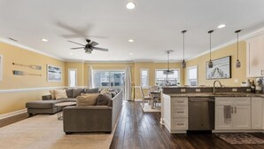 A spacious living room with a gray sectional sofa, a dining area, and a kitchen with white cabinets and a dishwasher. - Great Beach Condo Right Near the Boardwalk Awesome Rooftop Views of the Ocean (Wildwood)