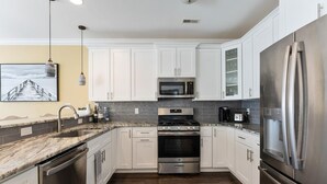 A modern kitchen with white cabinets, stainless steel appliances, a granite countertop, and a dark wood floor. - Great Beach Condo Right Near the Boardwalk Awesome Rooftop Views of the Ocean (Wildwood)