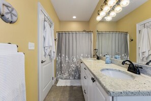 Une salle de bain avec deux lavabos, un rideau de douche orné de motifs floraux, un porte-serviettes et un miroir avec éclairage intégré.
