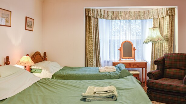 Een hotelkamer met twee bedden, een houten dressoir, een stoel, een spiegel en een raam met gordijnen.