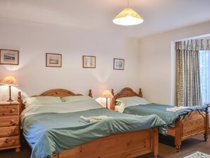 A bedroom with two wooden beds, a nightstand with a lamp, and framed pictures on the wall. - Pine Tree Cottage - UK45925 (Ballater)