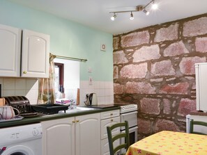 A kitchen with white cabinets, a washing machine, a stove, and a table with a yellow tablecloth.