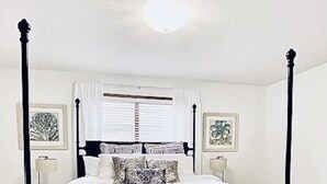 A four-poster bed with a white and black bedspread, flanked by two nightstands with lamps, in a room with wooden flooring and white walls. - Home Calls the Heart- 10 minutes to Mayo.  Split-level home with fenced-in yard. (Rochester)