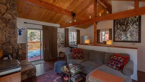 A cozy living room with a stone wall, wooden ceiling, and a large window. - Cozy Mountain Getaway in Arrowbear Lake, minutes from ski resorts. Pet-Friendly! (Running Springs)