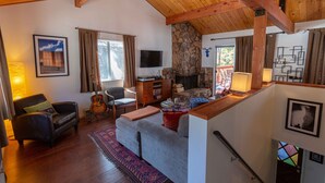 A cozy living room with a fireplace, wooden beams, a stone wall, a television, and a comfortable seating area. - Cozy Mountain Getaway in Arrowbear Lake, minutes from ski resorts. Pet-Friendly! (Running Springs)