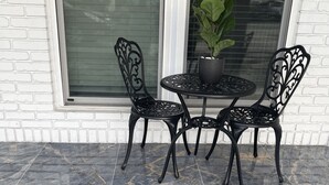 Un patio con una mesa y sillas de metal negro, una planta en maceta y un muro de ladrillo blanco.