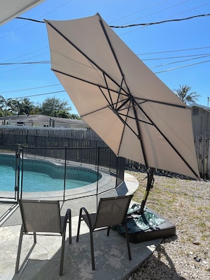 A poolside area with a covered seating area, a pool, and a fenced yard.