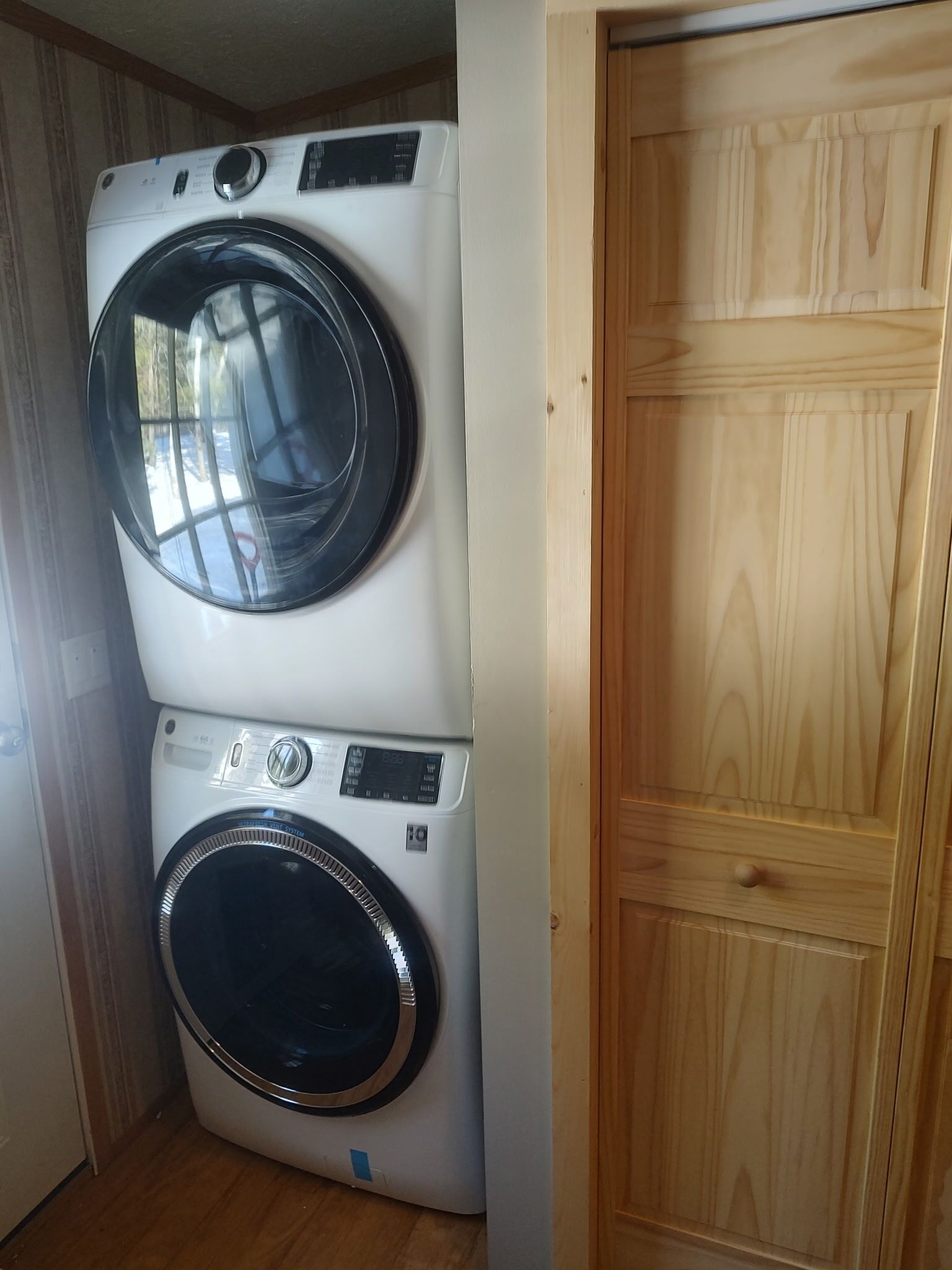 Lavatrice e asciugatrice affiancate in una stanza con rivestimenti in legno e una porta di legno.