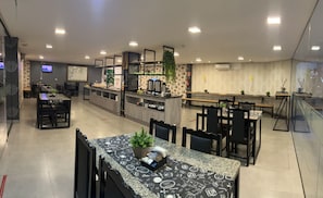 A modern restaurant with a central bar, multiple dining tables, and a kitchen area.