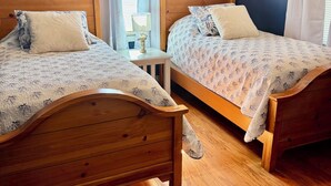 A room with two wooden beds, a small table with a lamp, and a window with curtains.