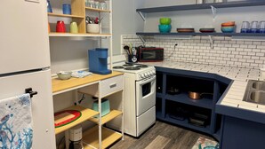 A kitchen with a refrigerator, stove, microwave, shelves with dishes, and a coffee maker.
