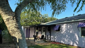 A house with a covered patio, a white picket fence, and a tree in the foreground.