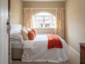 A bedroom with a bed, curtains, a window, and a view of buildings outside.